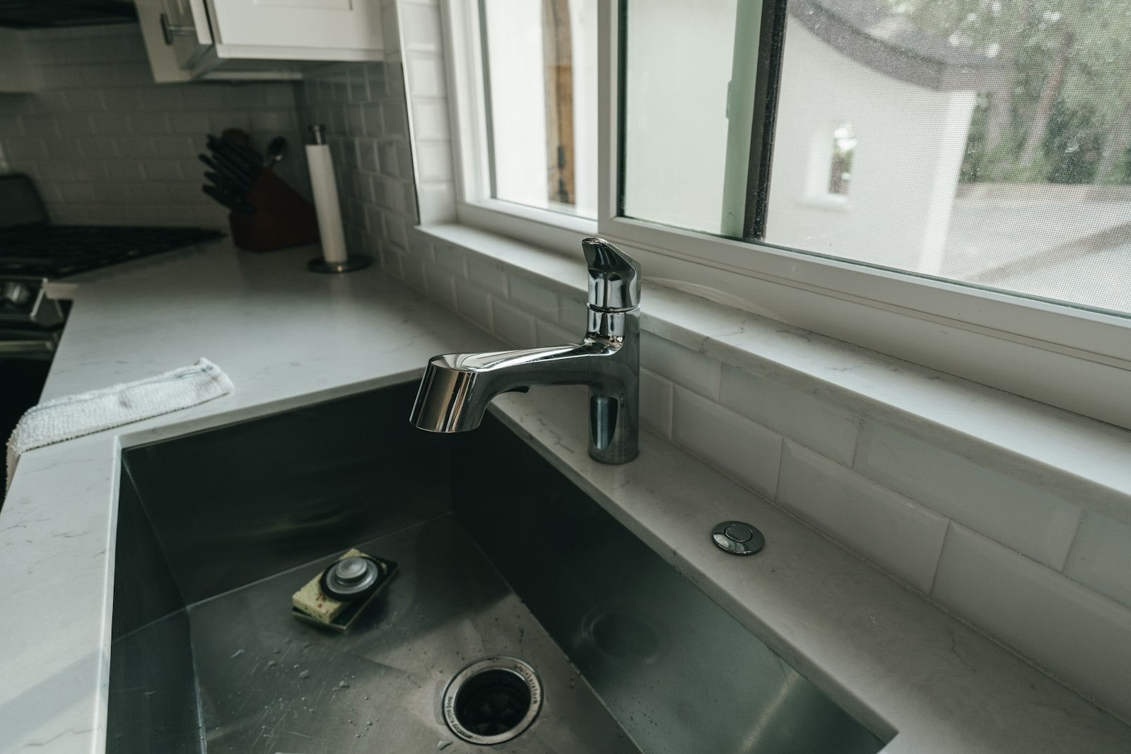 Stainless kitchen sink and faucet beside a window